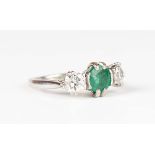 An 18ct white gold, emerald and diamond ring, claw set with the circular cut emerald between two