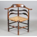A George III provincial elm and ash bow backed corner chair with a rush seat and wavy ladder back,