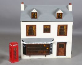 A modern doll's house shop, the tiled roof hinged to reveal a bedroom and bathroom, above an opening