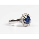 A white gold, sapphire and diamond cluster ring, claw set with the oval cut sapphire within a