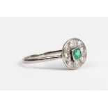 A white gold, emerald and diamond cluster ring, the central emerald mounted within a surround of