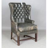 An early 20th century George III style buttoned dark green leather wingback armchair with brass