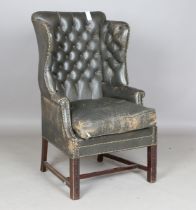 An early 20th century George III style buttoned dark green leather wingback armchair with brass