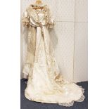 An early 20th century cream silk wedding dress with net and pearl appliqué borders and long train,