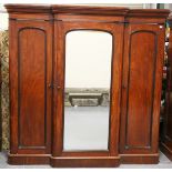 A Victorian mahogany breakfront wardrobe, fitted with a central mirrored door enclosing trays and