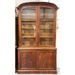 A mid-Victorian mahogany bookcase cabinet, the arched pediment above glazed doors and a pair of