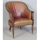 A George III mahogany framed tub back library armchair, upholstered in claret leather, raised on