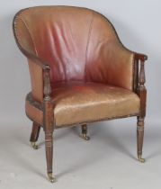 A George III mahogany framed tub back library armchair, upholstered in claret leather, raised on