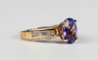 An 18ct gold, tanzanite and diamond ring, claw set with the oval cut tanzanite between baguette