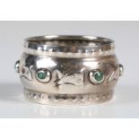 An Arts and Crafts silver and turquoise inset napkin ring, the central band decorated with a line of