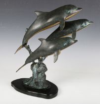 A late 20th century patinated bronze model group of three dolphins on an ebonized shaped wooden