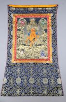 A Tibetan woven silk thangka, the central panel finely painted with a seated deity, 126cm x 80cm.