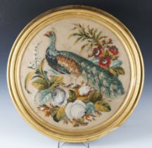 A Victorian wool and raised plush work tondo panel of a peacock standing within a floral surround,