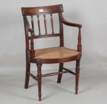 A late George III mahogany bar back elbow chair with a reeded spindle back and caned seat, raised on