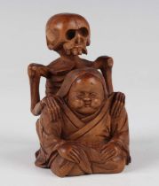 A Japanese carved boxwood okimono figure group by Ikko, Meiji period, modelled as a seated Okame