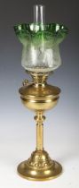 An Edwardian Arts and Crafts brass table oil lamp, the green tinted glass shade with acid etched