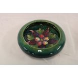A small Moorcroft pottery circular shallow bowl with floral decoration on green ground,