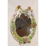 A 20th century German porcelain oval vanity mirror decorated in relief with two cherubs and flowers