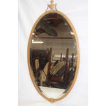 A bevelled oval wall mirror in gilt metal frame surmounted by a classical urn finial,