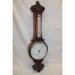 A good quality aneroid barometer with circular ceramic dial below thermometer in carved oak case