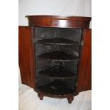 A 19th century oak corner cupboard with shelves enclosed by two curved panelled doors on turned