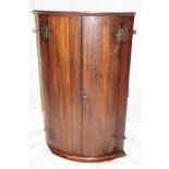 A 19th century oak hanging corner cupboard with shelves enclosed by a pair of curved panel doors