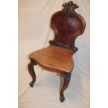 A Victorian carved mahogany hall chair with arched back and polished seat on scroll legs