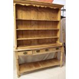 A rustic polished pine kitchen dresser with three drawers in the frieze and open pot boards with
