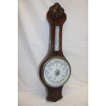 An aneroid barometer with ceramic circular dial below thermometer in carved oak case