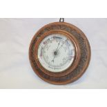 An old aneroid barometer with ceramic circular dial in carved oak circular case