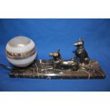 An Art Deco table lamp in the form of two Alsatian dogs before a glass sphere on rectangular marble