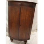 A 19th century oak corner cupboard with shelves enclosed by two curved panelled doors on turned