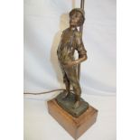 A bronzed spelter table lamp in the form of a young boy beneath a scroll lantern with glass shade