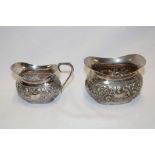A silver plated oval milk jug with raised scroll decoration and matching sugar basin