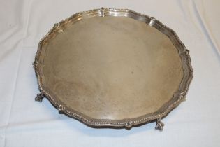 A George V silver circular tray with pie-crust edge on four claw and ball feet,