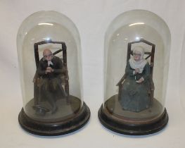 A pair of Continental china figures of elderly seated males and females contained within glass