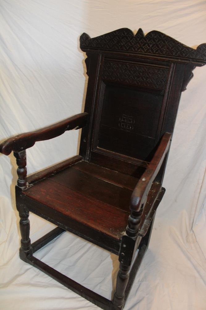 A 17th century carved oak carver armchair with arched panelled back and planked seat on turned