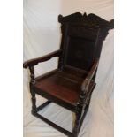 A 17th century carved oak carver armchair with arched panelled back and planked seat on turned
