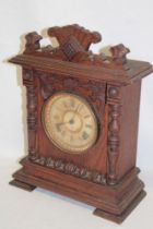 An old Continental mantel clock with decorated circular dial in stained pine carved case