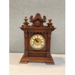 A circa 1900 oak cased bracket clock, Roman chapter ring, carved and finial top, with pendulum