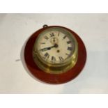 A brass cased ship's clock mounted on hardwood plaque