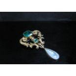 An ornate pendant/brooch set with green paste stones and hung with a blister pearl droplet, 7.5cm