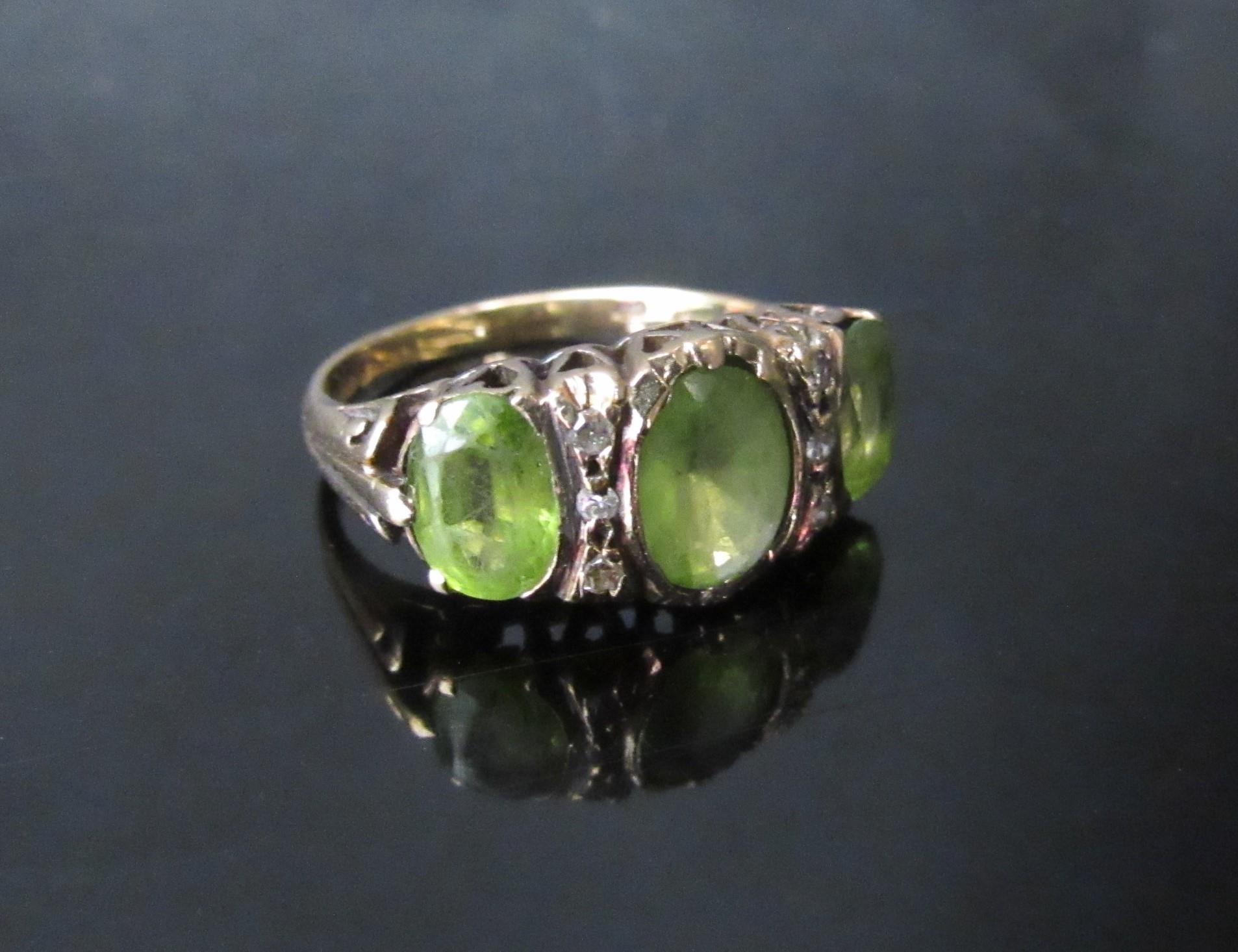 A 9ct gold ring with three oval peridots, the central stone flanked by three diamonds. Size N/O, 4. - Image 2 of 3