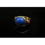 A gold ring, unmarked, set with oval lapis lazuli, flanked by coral in rubover setting, shank