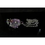 An ornate pendant with central large carved amethyst flower with metal work scrolls of precious