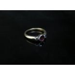 A 9ct gold ruby and diamond ring the central circular ruby flanked by diamonds in rubover setting.