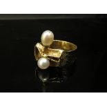 A gold modernistic ring set with two pearls on a textured band with pierced abstract bow design,