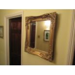 A gilt ornate mirror with bevelled glass, floral embellishment 67cm x 57cm