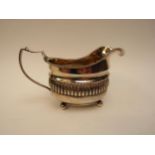 A George III silver cream jug with gadrooned rim, ball feet, makers mark I.B. London 1815,