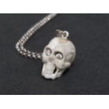 A carved pendant in the form of a human skull, set with brilliant white stone eyes and set on a